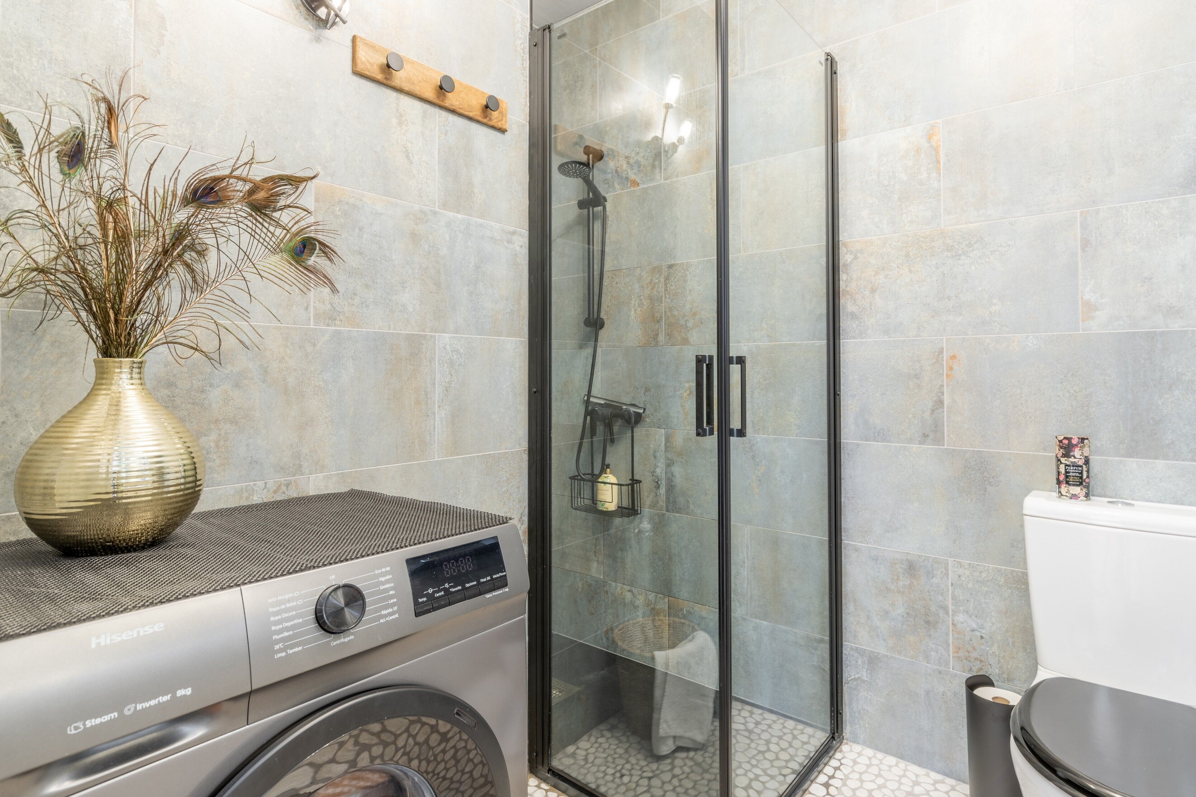 A modern bathroom with a glass shower enclosure, a washing machine, and a decorative vase.