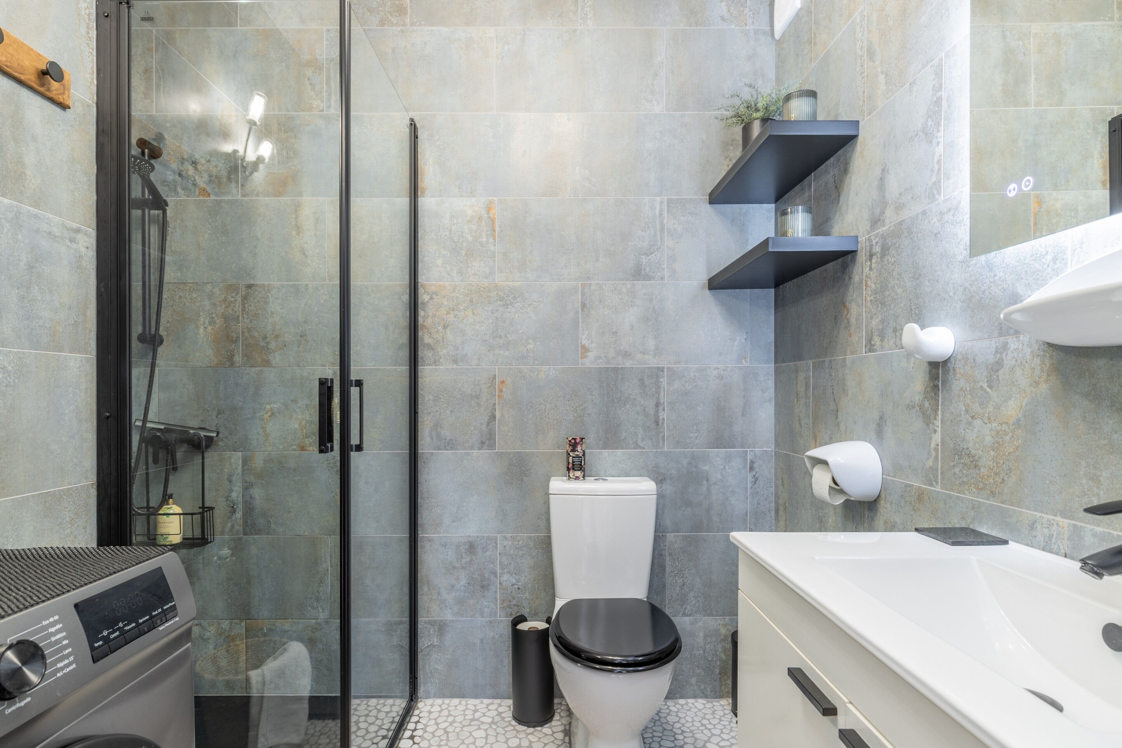 A modern bathroom with a glass shower enclosure, a toilet, a sink, and a built-in washing machine.