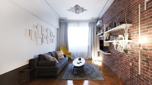 A modern living room with a sofa, armchair, and coffee table. A brick wall and a chandelier are visible. - Centrally Athenian Apartment (Athens)