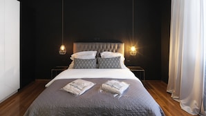 A modern bedroom with a tufted headboard, two bedside lamps, and a large bed with a grey quilt. - Centrally Athenian Apartment (Athens)