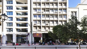 A multi-story building with balconies, air conditioning units, and a coffee shop on the ground floor. - Centrally Athenian Apartment (Athens)