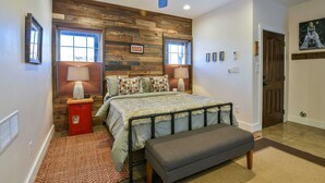 A bedroom with a wooden wall panel, a bed with a grey bench, two bedside lamps, a red storage unit, and a ceiling fan. - Moab Digs #1 - Your Downtown Basecamp! (Moab)