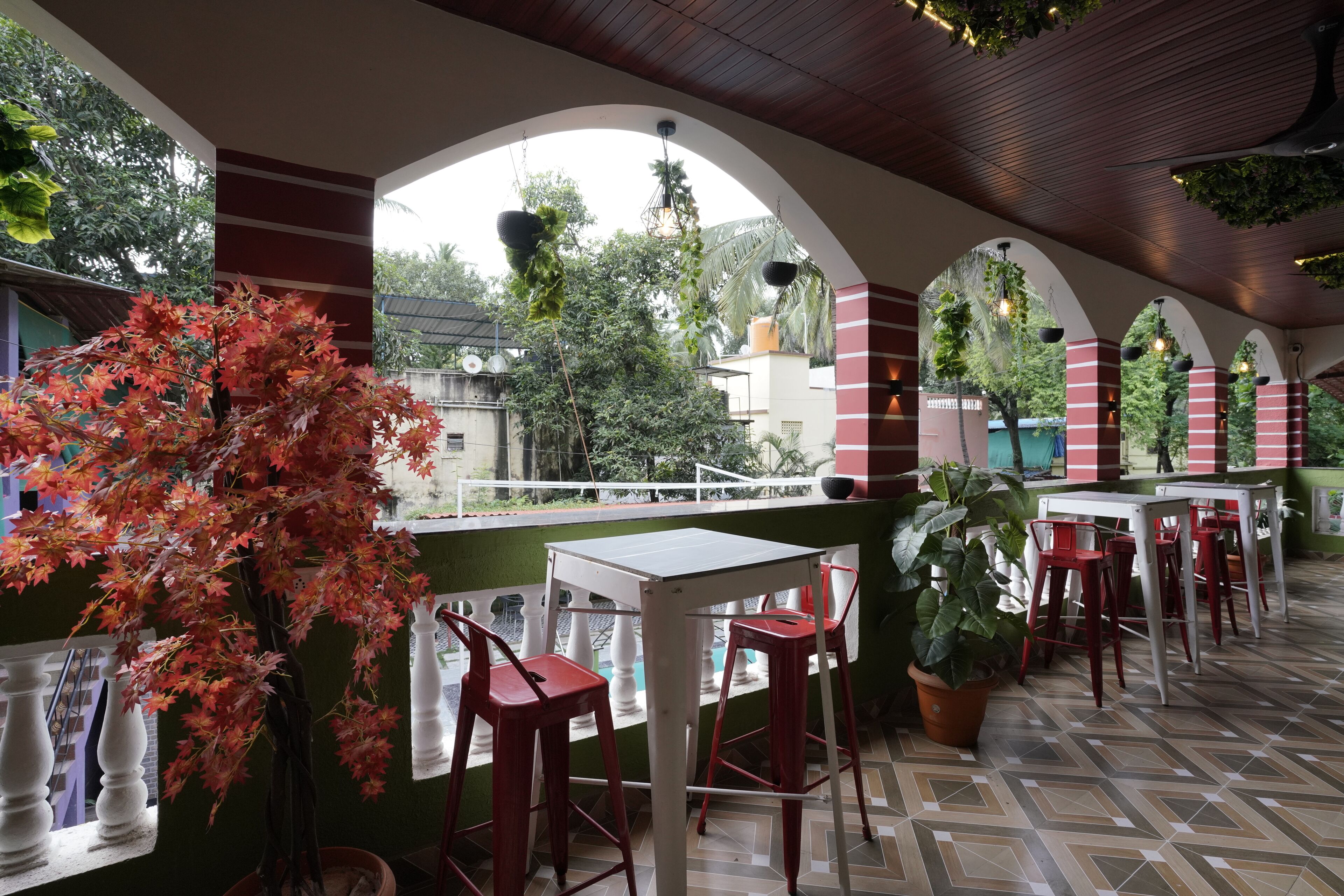 An outdoor cafe area with tables and red chairs, surrounded by arches and potted plants.