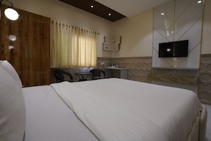 Habitació d'hotel amb un llit gran, una taula de treball amb dues cadires, una televisió penjada a la paret i una finestra amb cortines.