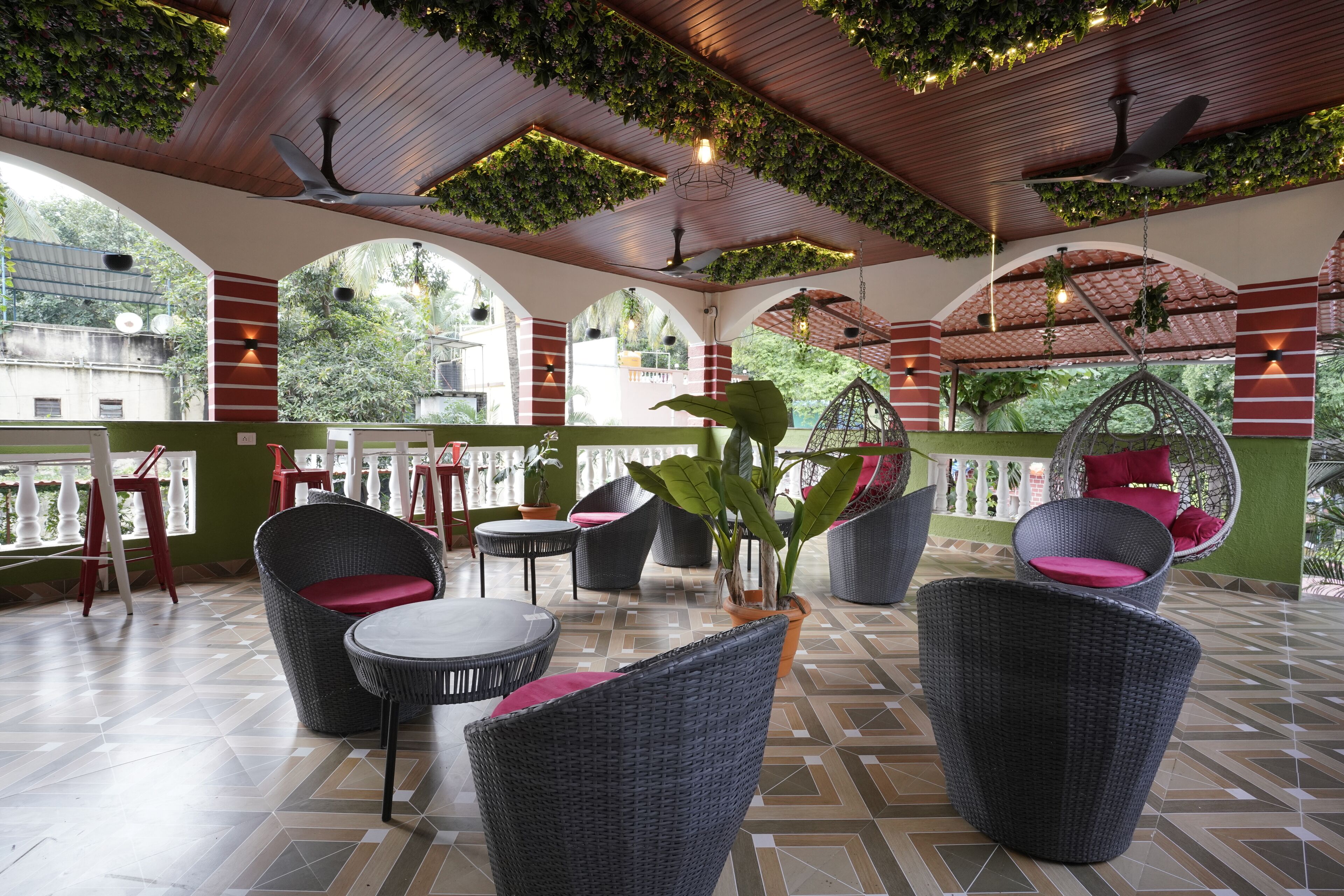 A covered outdoor seating area with wicker furniture, potted plants, and a view of greenery.