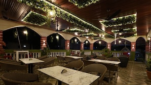 Un espace extérieur aménagé pour les repas, avec des meubles et des tables en osier, entouré d’arcades et agrémenté de plantes en pot.