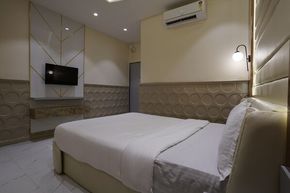 Habitación de hotel con cama, televisor de pantalla plana en la pared, unidad de aire acondicionado y lámpara.