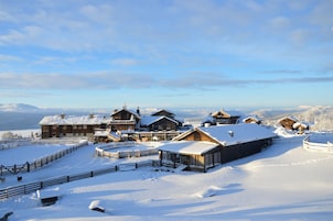 A snow-covered lodge with multiple wooden cabins, a fenced yard, and a clear view of the surrounding mountains.