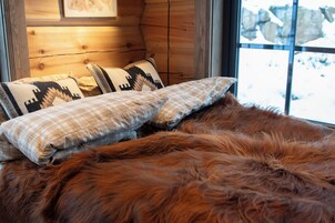 A bed with a brown fur throw, plaid pillows, and a wooden headboard.