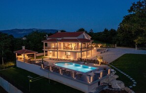 Una casa de dos plantas con piscina, un patio cubierto y un jardín ajardinado.