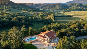 Une grande maison avec une piscine, entourée d’une végétation luxuriante et de montagnes.