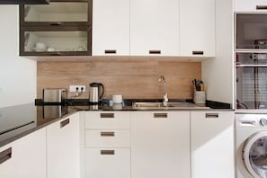 Una cocina moderna con horno empotrado, cafetera y lavadora.