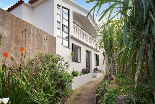 Un edificio blanco con balcón, rodeado de follaje y plantas.