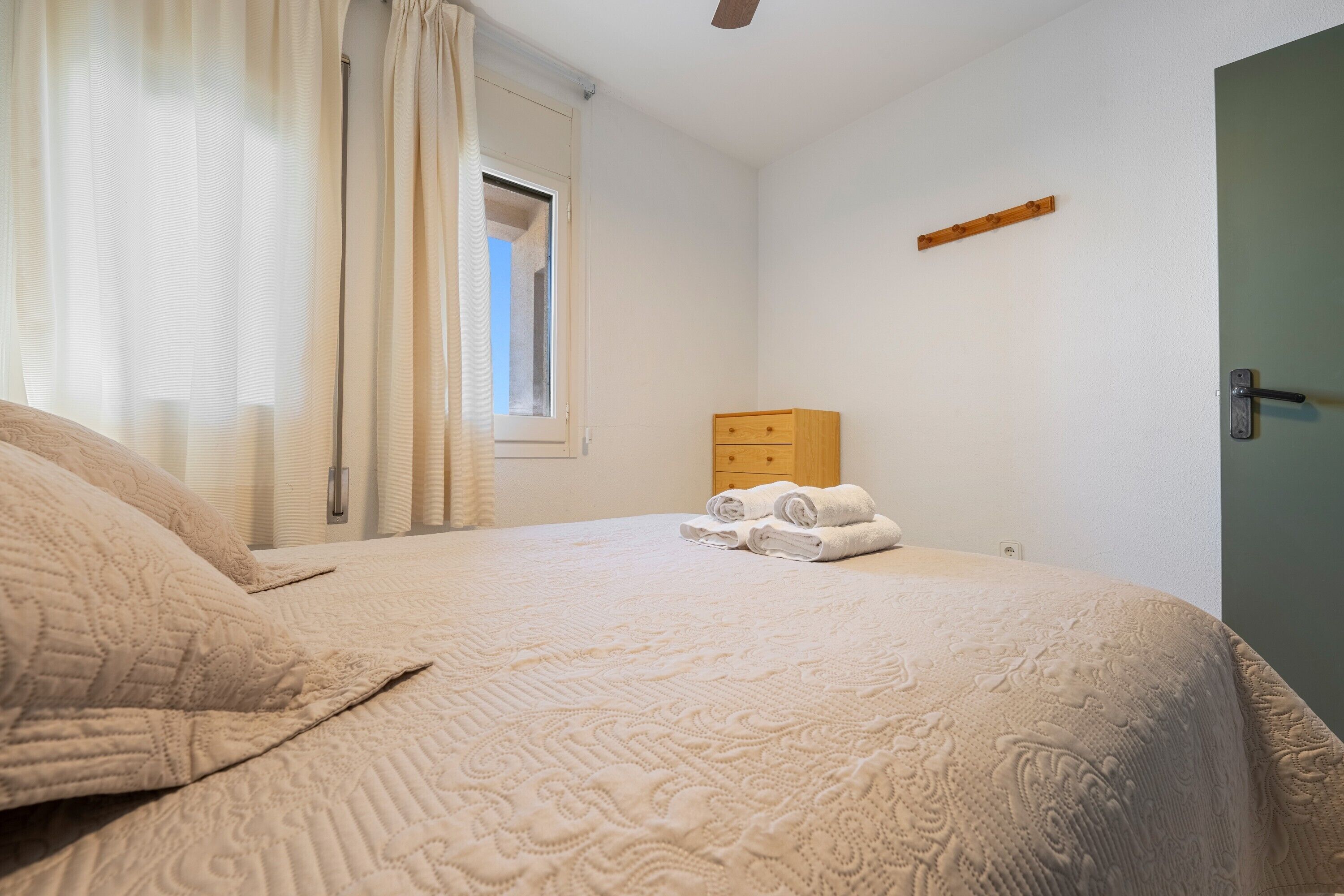 Un dormitorio con cama, cómoda de madera, ventana con cortinas y puerta.