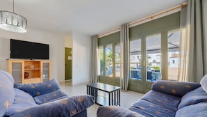 Una sala de estar con un conjunto de sofá, un televisor, una mesita y vistas amplias por los ventanales.