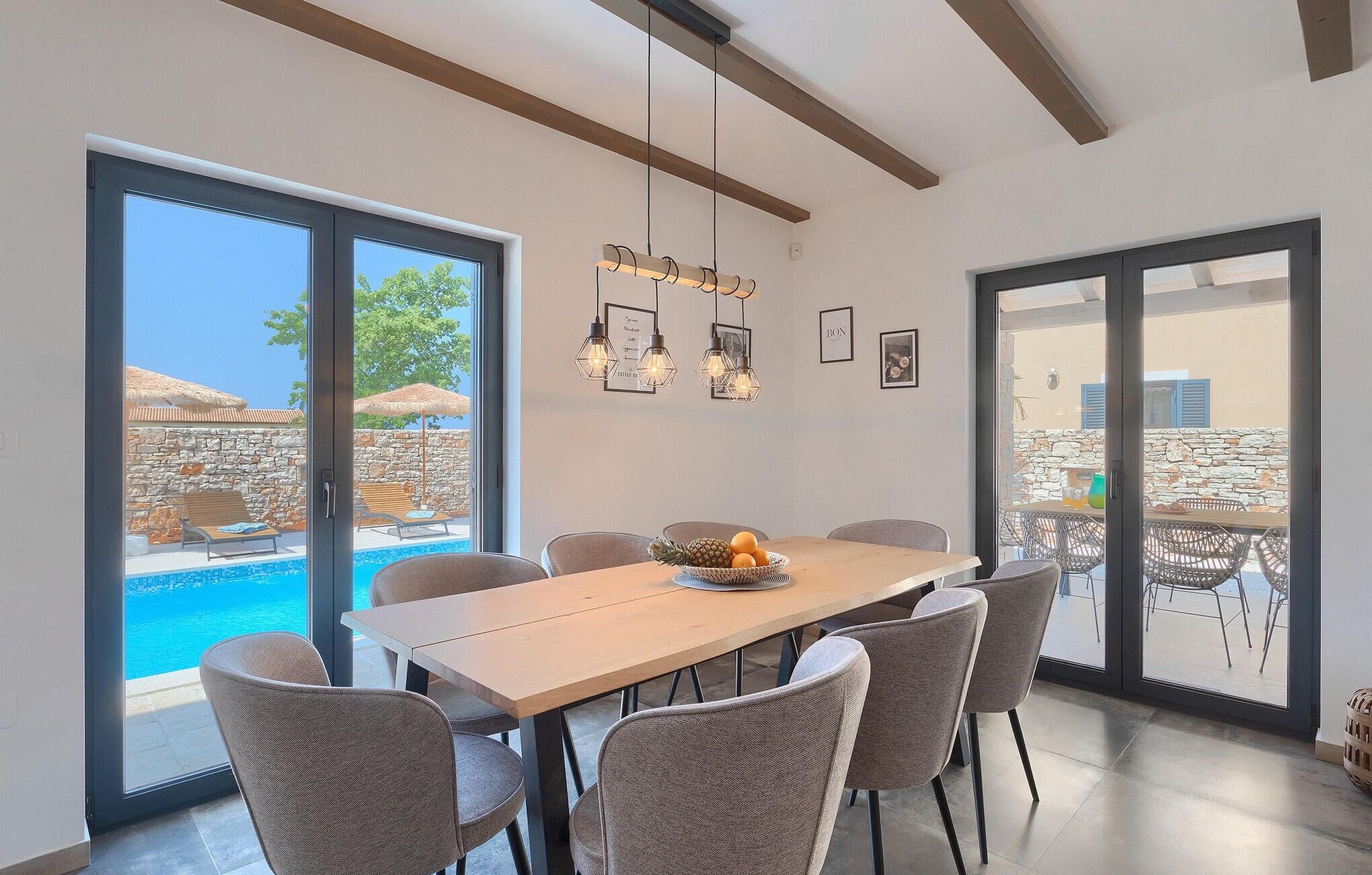 A dining area with a large table and chairs, a view of a swimming pool, and a stone wall.