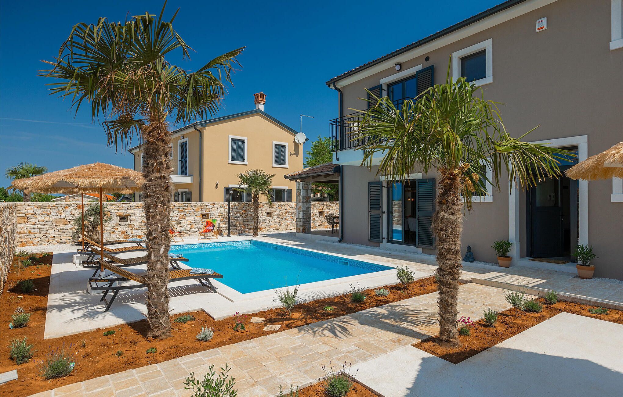 Un espace aménagé au bord de la piscine, avec une piscine, des palmiers et un mur en pierre.