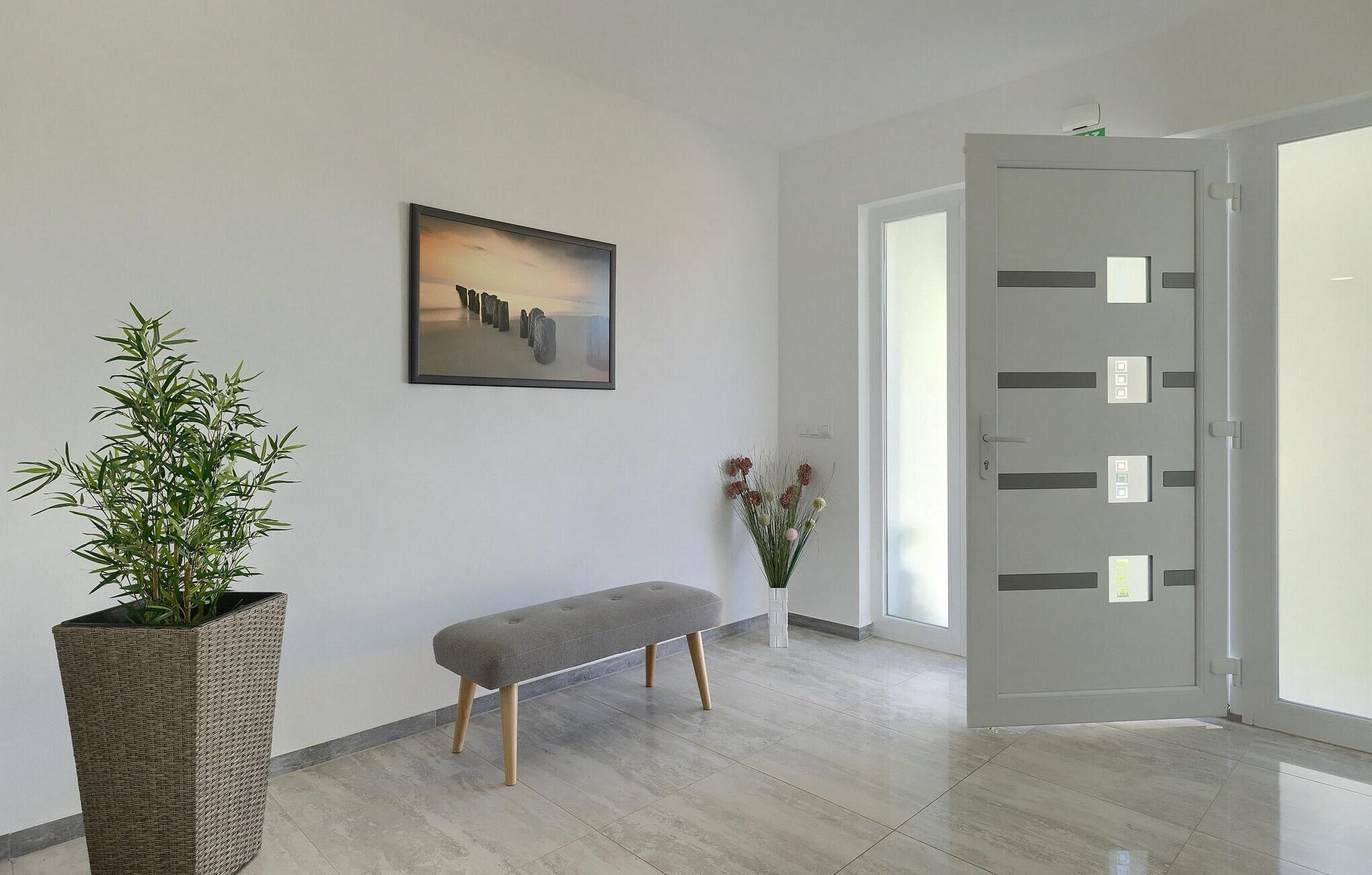 A modern hallway with a bench, a potted plant, a framed picture, and a door with multiple locks.