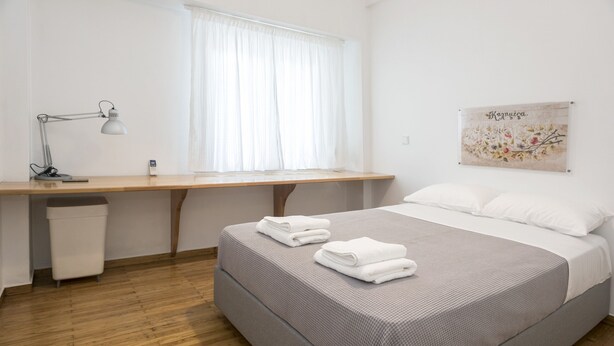 A neatly arranged bedroom with a bed, a desk, and a window. - Colourful Apartment Under the Cropolis (Athens)