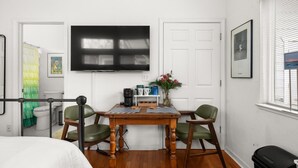 Een kamer met een bed, een houten tafel met stoelen, een aan de muur bevestigde televisie en een raam met jaloezieën.