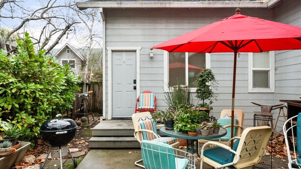 Een terras met tuinmeubilair, een rode parasol en potplanten.