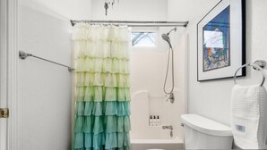 Een badkamer met een douchegordijn in niveaus, een bad, een toilet en een wastafel.