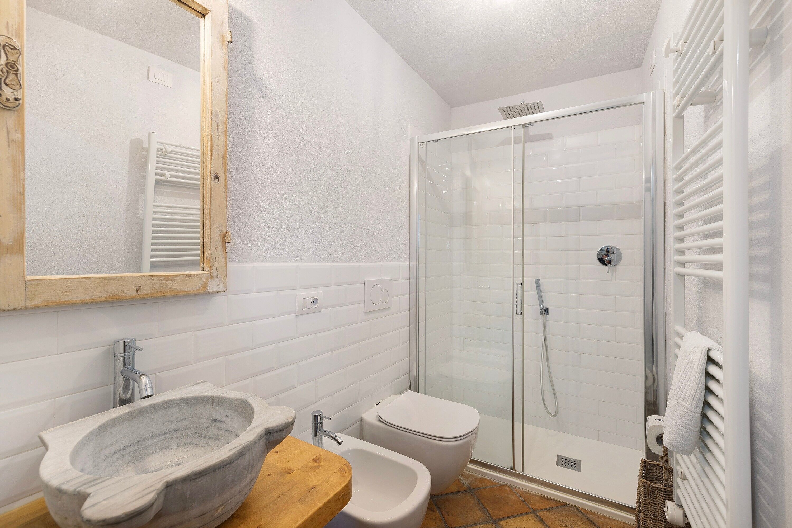 Un baño con un lavabo de piedra, encimera de madera, inodoro, ducha con cerramiento de vidrio y un perchero para toallas.