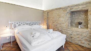 A bed with white linens and towels, a white bedside table, and a stone wall with a fireplace.