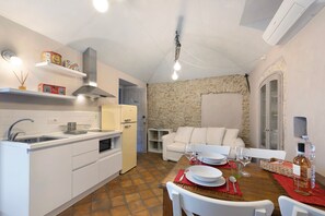 Cocina compacta con muebles blancos, estufa integrada y comedor con mesa lista para dos.