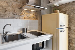 Una cocina con un lavamanos de acero inoxidable, un microondas integrado y un refrigerador color crema.