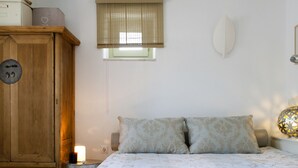 Un dormitorio con una cama, un armario de madera, una lámpara de noche y una ventana con persianas.