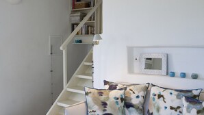 Una sala de estar con un sofá blanco, cojines estampados, una mesa de centro de madera, una escalera blanca y una estantería.