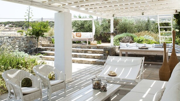 Un área de estar al aire libre con mobiliario blanco, una pérgola arriba y vistas del paisaje.