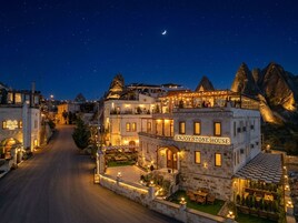 Una casa de piedra con un cartel que dice 'ENJOY STONE HOUSE', rodeada por una calle y montañas, de noche.