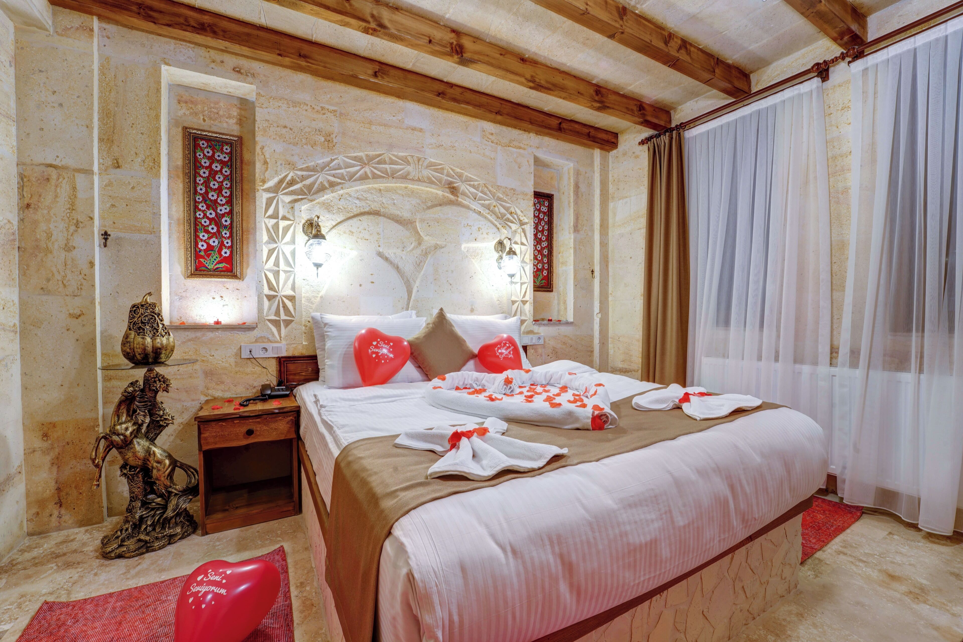 Quarto de hotel com cama grande, mesa de cabeceira, estátua decorativa e janela com cortinas.