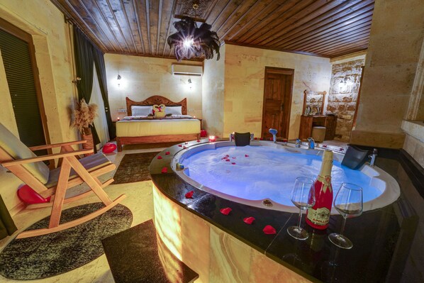 Une chambre avec un plafond en bois, un lit doté d’une tête de lit en bois, un jacuzzi, un fauteuil et une bouteille de champagne.