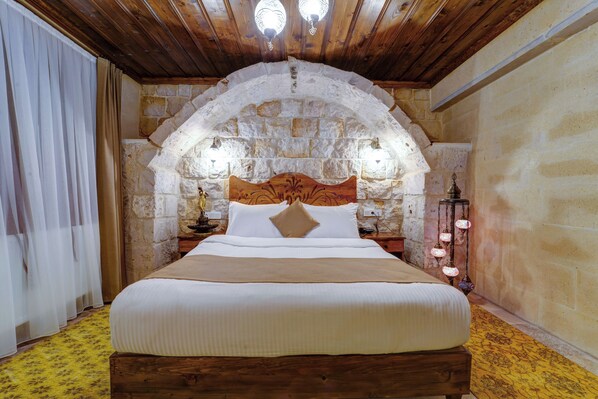 A bedroom with a stone arch ceiling, a wooden bed frame, and a nightstand with a lamp. - Enjoy Stone House (Nevsehir)