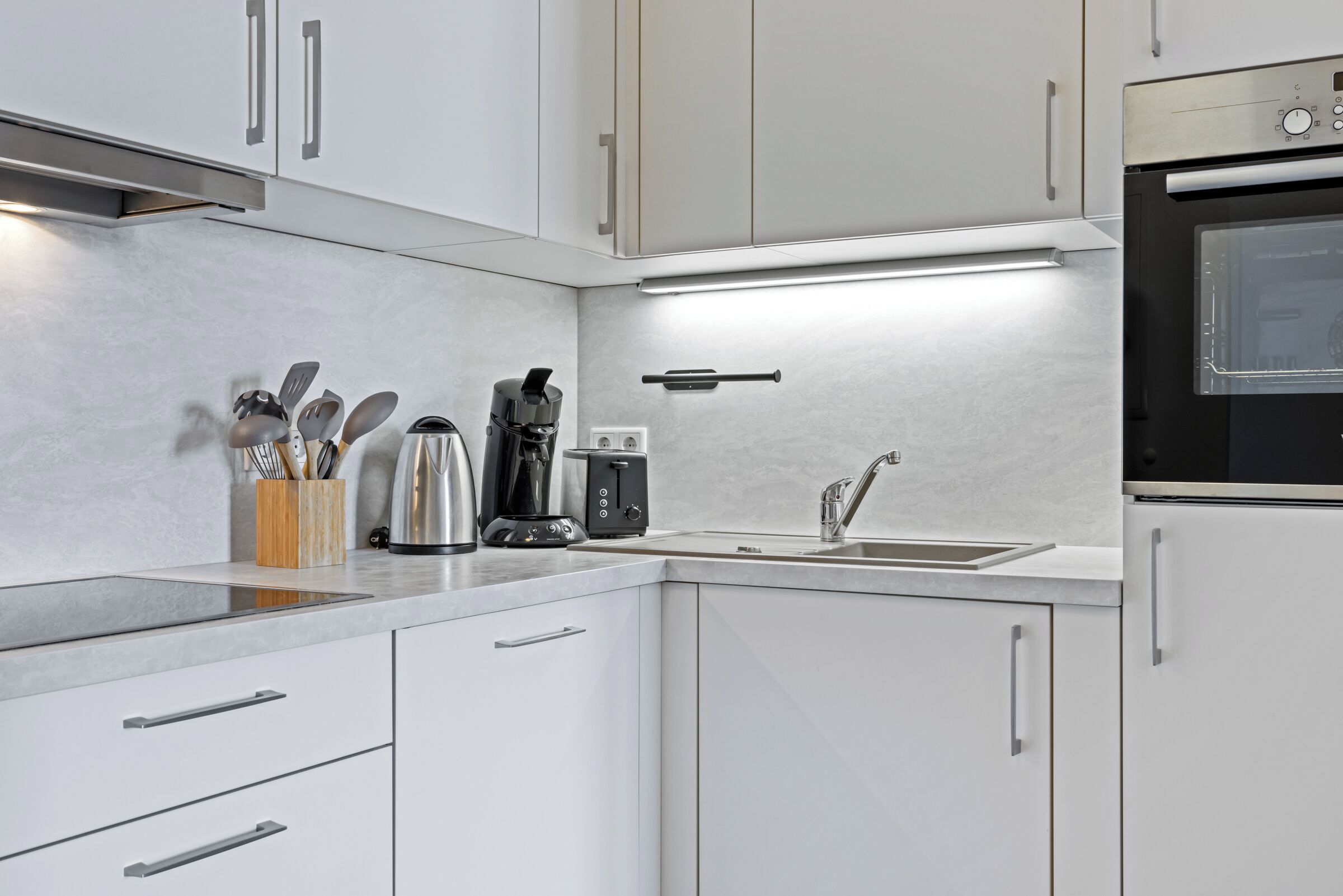 Una cocina moderna con armarios blancos, electrodomésticos de acero inoxidable y un horno empotrado.