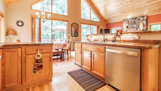 Un'ampia cucina con mobili in legno, lavastoviglie e grandi finestre che offrono luce naturale e vista sull'esterno.