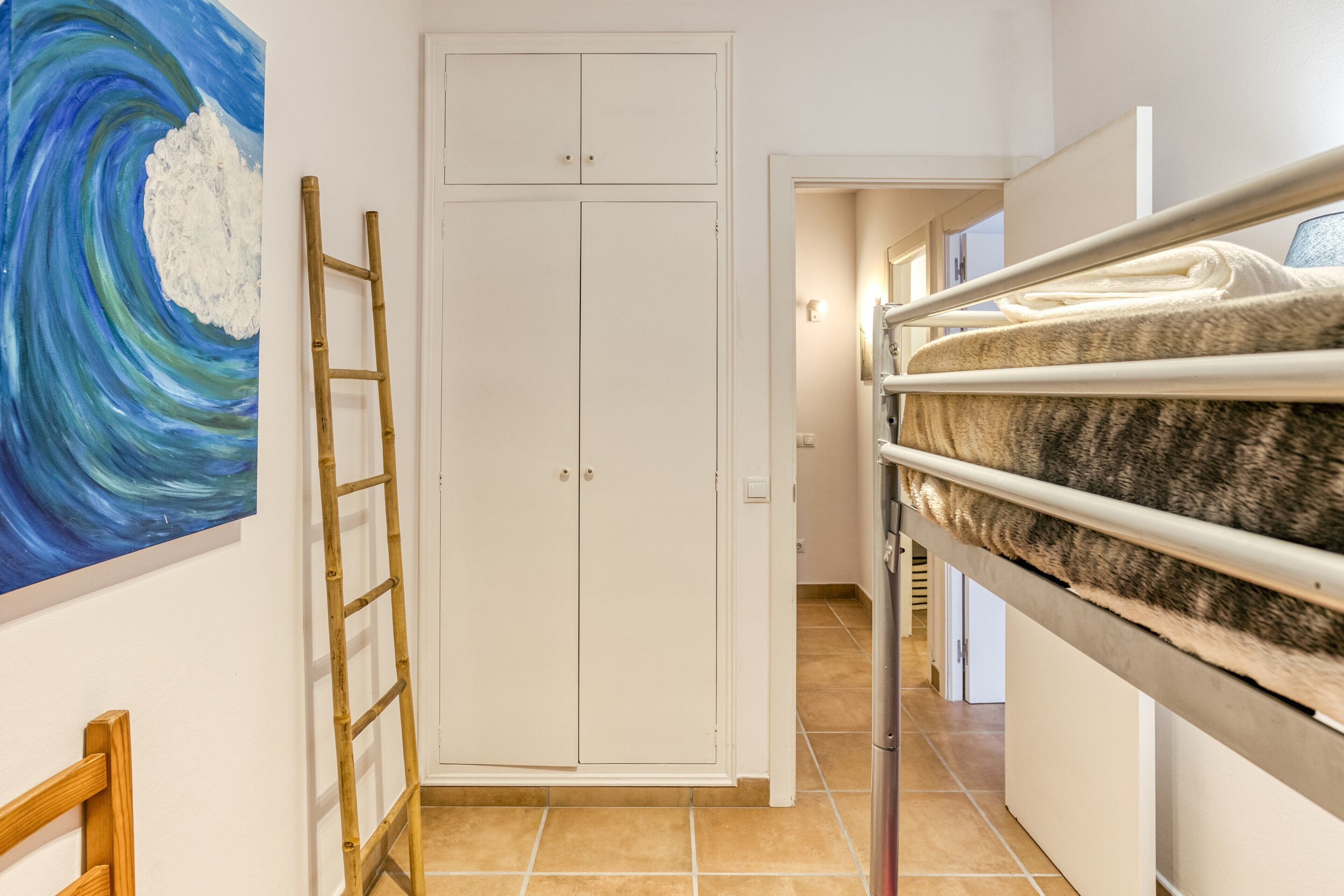 A room with a bunk bed, a white wardrobe, a ladder, and a painting on the wall.