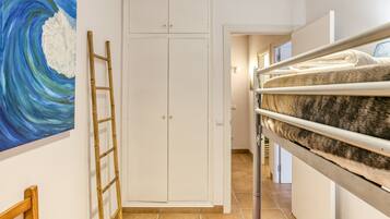 A room with a bunk bed, a white wardrobe, a ladder, and a painting on the wall.
