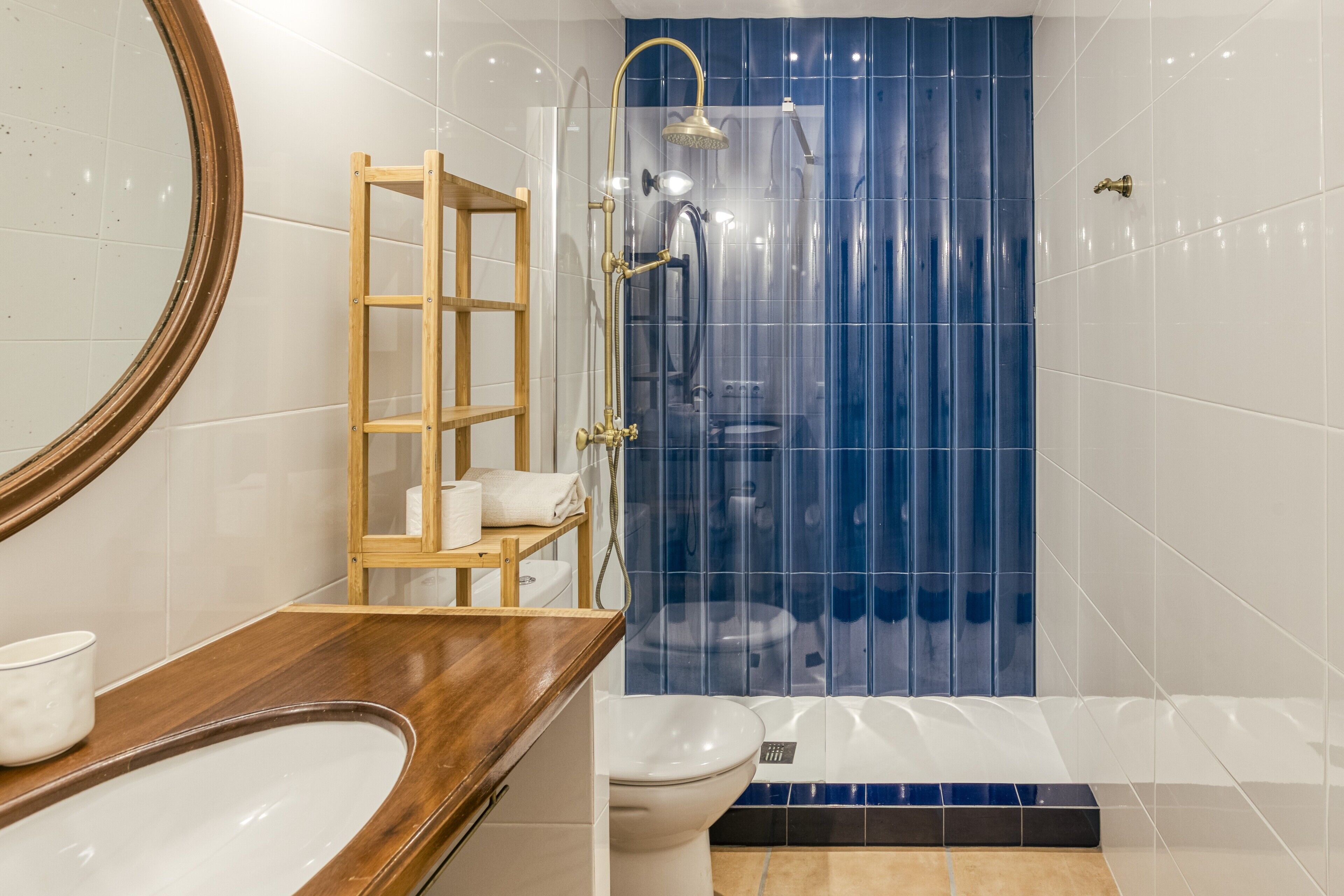 A bathroom with a wooden vanity, a toilet, a shower with a blue curtain, and a mirror.