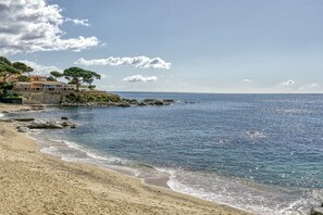 Ein Strand mit klarem Wasser, einer felsigen Küste und Gebäuden im Hintergrund.