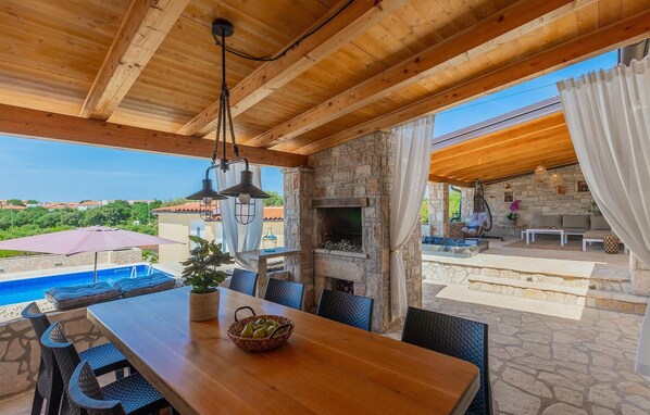 Enjoy al fresco dining with a view of the pool and surrounding landscape from this outdoor dining area, featuring a fireplace and comfortable seating.