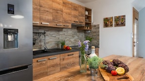 A modern kitchen with wooden cabinets, a stainless steel refrigerator, a water dispenser, and a wooden countertop with fresh produce and herbs. - Villa Kalista Istriana (Pula)