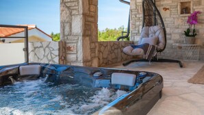 A hot tub with a stone wall backdrop, a hanging chair, and a view of greenery. - Villa Kalista Istriana (Pula)