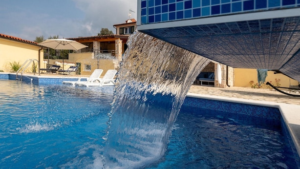 A swimming pool with a water feature, lounge chairs, and a building with a tiled roof. - Villa Kalista Istriana (Pula)