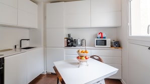A compact kitchen with white cabinetry, a white countertop, and a two-tiered fruit basket on the table. - Culture and Colour, by Veeve (Paris)