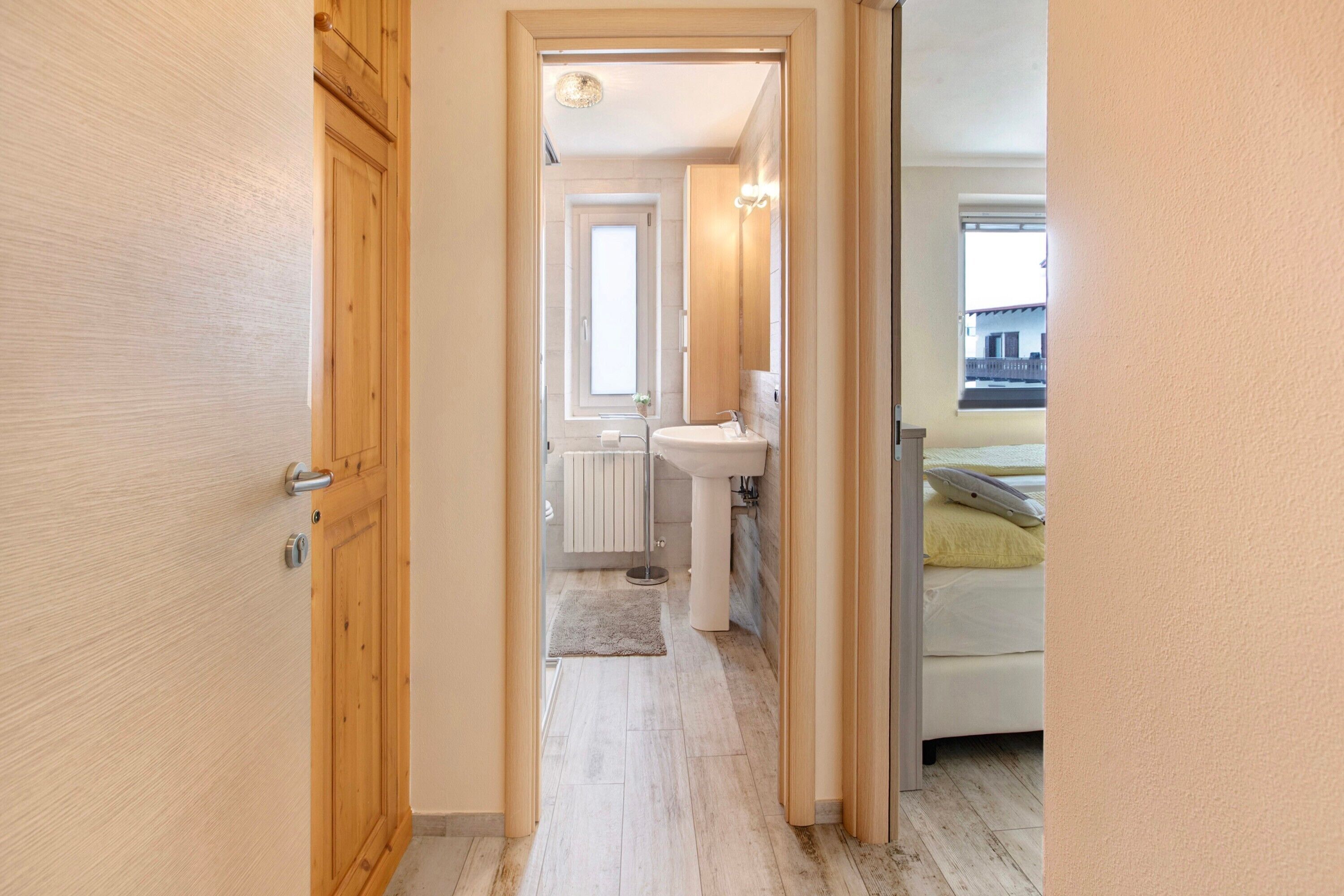 Un couloir menant à une salle de bain avec une fenêtre, un radiateur et un lit avec des oreillers.