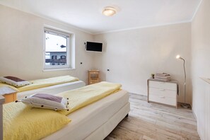 Un dormitorio con dos camas, televisión, mesita de noche, lámpara y ventana.